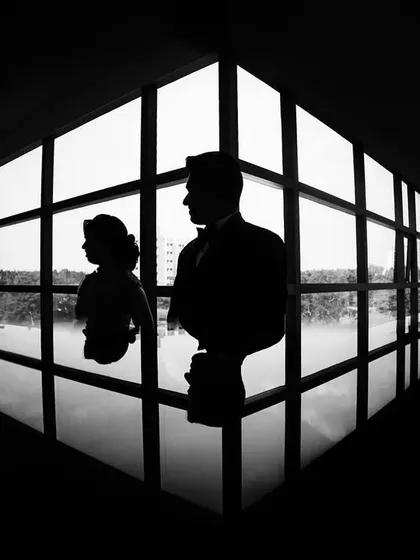 A powerful silhouette of the couple against a large window. This black and white shot uses reflection and symmetry to create a striking and artistic wedding portrait.