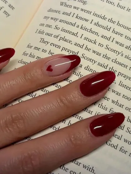 A classic Valentine's look. Deep red nails with a single accent nail featuring a sheer base and a tiny heart.