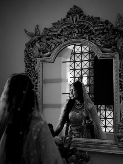 A black and white reflection shot of the bride looking at herself in an ornate mirror.