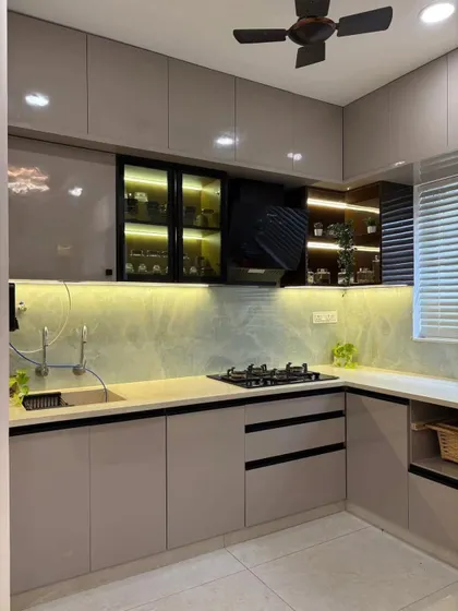 Another angle of the beige and white dual-tone kitchen, highlighting the L-shaped layout that provides an efficient work triangle. The under-cabinet lighting ensures the countertop is well-lit for food prep.