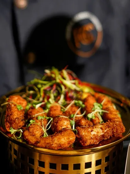 A close-up of a platter of golden-fried appetizers, garnished with fresh microgreens. The dish is served in a beautiful brass bowl, showcasing our use of luxury serveware for even the simplest of dishes.
