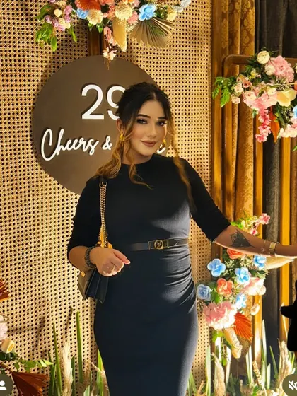 A guest enjoying the ambiance at a 29th birthday party we styled. The backdrop features a natural cane texture, a custom "29 Cheers & Shine" sign, and colorful floral accents.