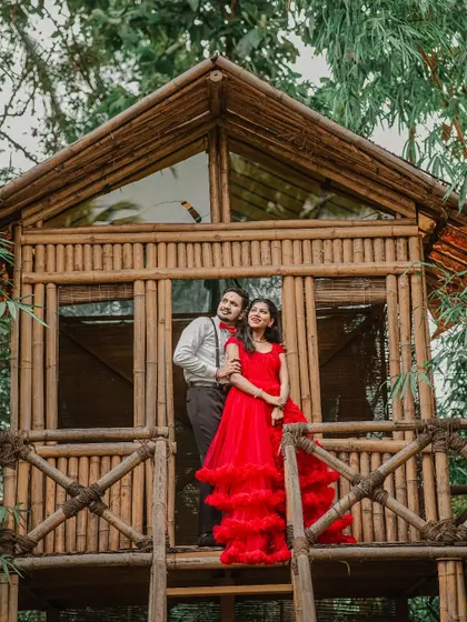 A romantic pose on a treehouse balcony. The red ruffled gown and the man's formal attire with a bow tie create a storybook scene.
