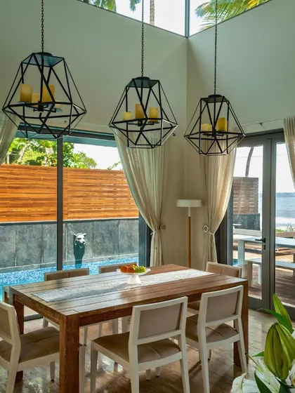 This dining room in a Goa residence features a double-height ceiling with a skylight, flooding the space with natural light. The design connects directly to the poolside, embodying a relaxed, holiday-living ethos.
