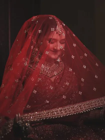 A classic bridal portrait showing the bride under her red veil. The soft lighting and her gentle smile create a timeless and serene image, full of grace and beauty.