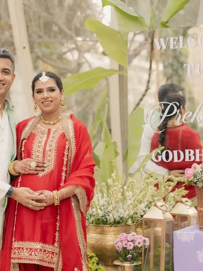 The happy couple at the entrance of their Godh Bharai ceremony, featuring a custom acrylic welcome sign.