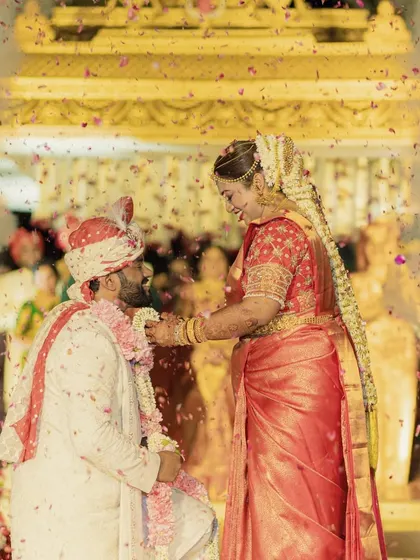 A beautiful moment from a South Indian wedding, as the bride and groom exchange garlands. The air is filled with a shower of petals, capturing the joy and celebration of the union.