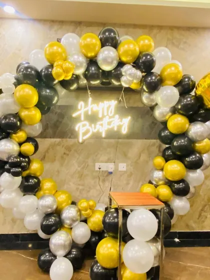 A birthday balloon ring in black, white, and gold, with a "Happy Birthday" neon sign.