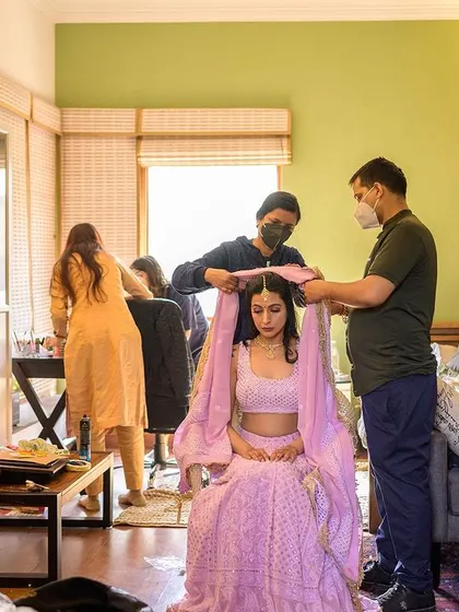 A behind-the-scenes look at the bride getting her dupatta set, surrounded by her hair and makeup team.