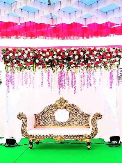 A classic reception stage with a royal touch. The ornate golden sofa is complemented by red and white floral arrangements and delicate hanging flower strings against a draped backdrop.