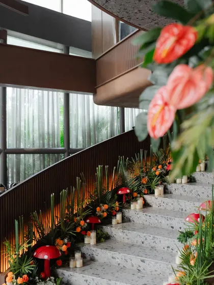 The staircase decorated with a lush runner of tropical greens, orange florals, and red mushroom props, lit by the warm glow of candles.