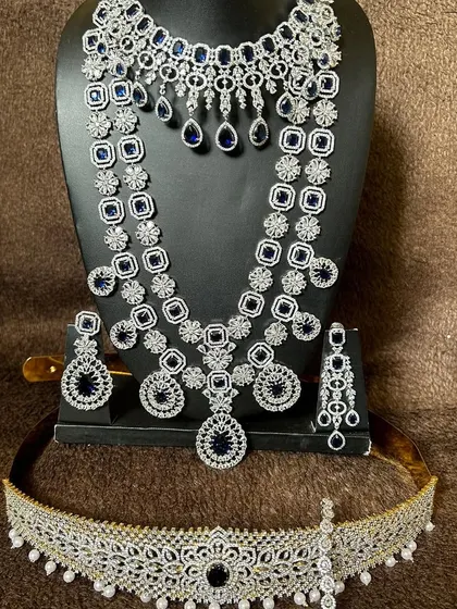 This modern CZ stone set features striking blue sapphire-like stones. The rental includes a choker, a long necklace, earrings, and a matching vaddanam.