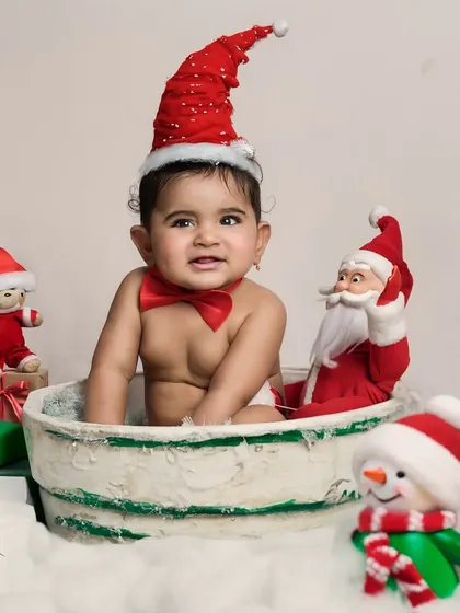 A festive Christmas-themed cake smash! A baby in a Santa hat and bow tie sits in a tub, surrounded by holiday decorations.