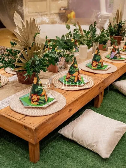 A low-seating arrangement for kids, with a wooden table, cushions, and themed party hats and plates for a jungle picnic feel.
