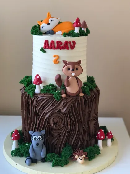 A charming two-tiered woodland animals cake, with a tree stump base and adorable creatures like a fox, squirrel, and raccoon.