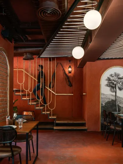 The sleek, minimalist staircase at 'Chambal' is a design feature in itself. Its delicate metalwork contrasts with the earthy red walls and rustic artifacts, creating a point of visual interest.