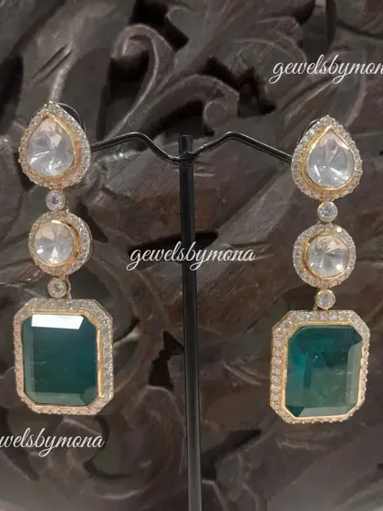 These long drop earrings feature a line of polki stones culminating in a large, rectangular emerald. They are the epitome of elegance and are perfect for a sophisticated evening look.