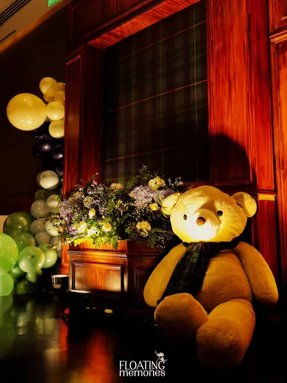 A close-up of one of the friendly teddy bears that greeted guests. Dressed in a tartan scarf, it perfectly embodies the charming and classic spirit of the 'Polo Club' first birthday theme.
