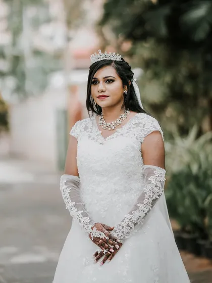 A medium shot of the bride, her hands gently clasped, showcasing her full bridal look against a soft green background.