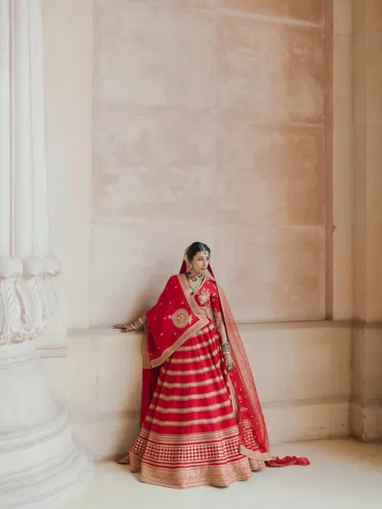 A regal portrait of Nikki in her red Sabyasachi lehenga. The architectural details of the palace provide a grand and fitting backdrop.