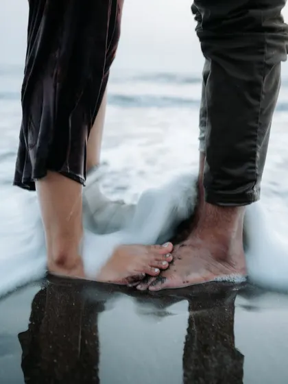 A creative close-up focusing on the couple's feet in the ocean surf, symbolizing their journey together. It's the small, artistic details that make a pre-wedding album special.