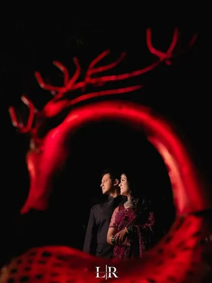 A creative portrait of a couple framed by a red, illuminated deer sculpture, creating a unique and artistic image.