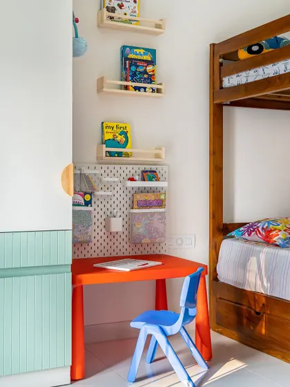 A close-up of the study area in the kids' room, with a bright red table and blue chair, and a pegboard organizer for art supplies.