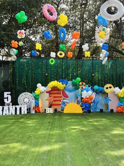 Another fantastic pool party setup, with a wide lawn, a lit-up number '5', and balloons shaped like pool floats hanging in the air.
