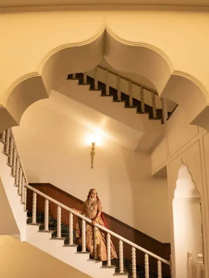 The bride descending the stairs, a moment of quiet elegance and anticipation before she meets her groom. The architecture frames her beautifully, creating a dramatic portrait.