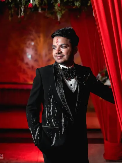 A close-up portrait of the groom against a vibrant red backdrop. His slight smile and confident pose make for a strong and stylish engagement photo.