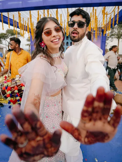 Fun and playful, this couple shows off their mehndi-stained hands to the camera. Their sunglasses and big smiles capture the carefree spirit of the Haldi ceremony.