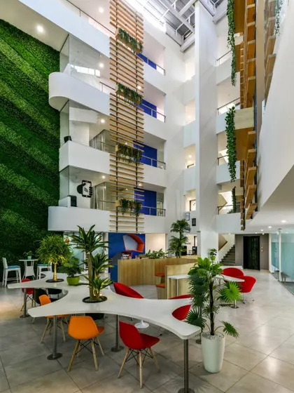 A view of the former hotel lobby, now a co-working common space. The towering green wall is the dominant feature, complemented by plant-integrated furniture.