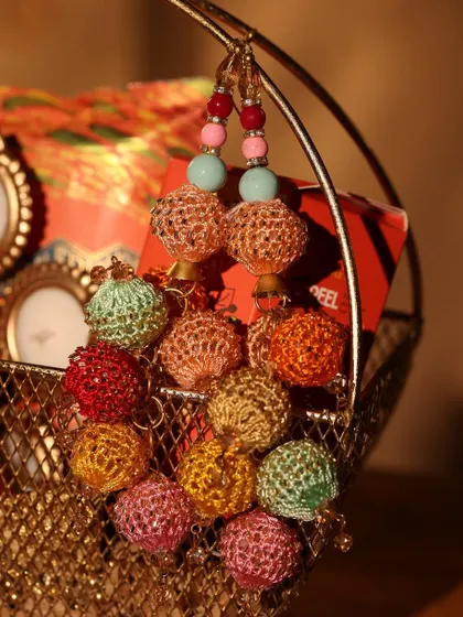 This traditional Diwali hamper is presented in a golden mesh basket. It features colorful latkans, adding a beautiful ethnic touch to the gift.