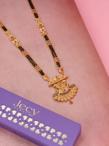 This image pairs a traditional gold mangalsutra with its modern purple packaging. The contrast between the traditional jewelry and the contemporary box creates a visually interesting story.