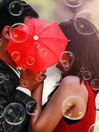 A creative pre-wedding shot with the couple sharing a kiss behind a bright red umbrella, surrounded by bubbles.