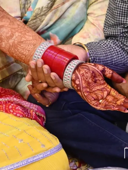 A beautiful shot of the bride's hand with the deep henna stain, holding her partner's hand. The rich color of the mehandi complements her red chooda bangles perfectly.