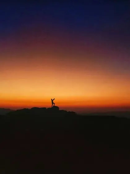 A silhouette of a person on a hilltop against a vibrant orange and purple sunset. A frame filled with emotion and the beauty of solitude.