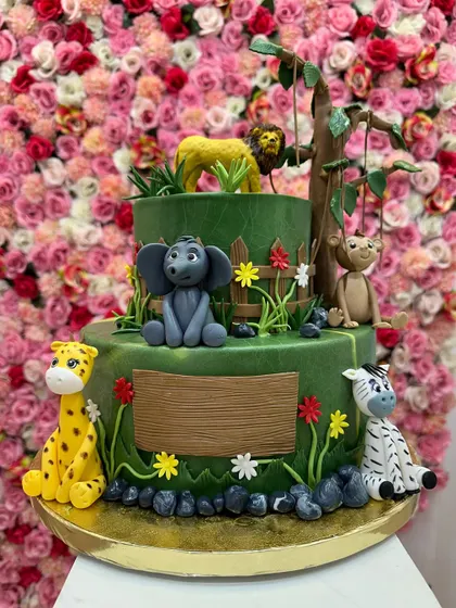 A beautiful two-tiered jungle cake with a rich green fondant. The hand-sculpted animals, including a lion, elephant, and giraffe, are placed in a charming forest scene.