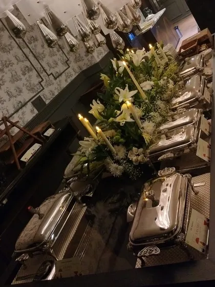 An angled shot of the candlelit buffet, showing the reflection of the elegant setup on the glossy table. The combination of flowers, candles, and polished silver creates a truly luxurious feel.