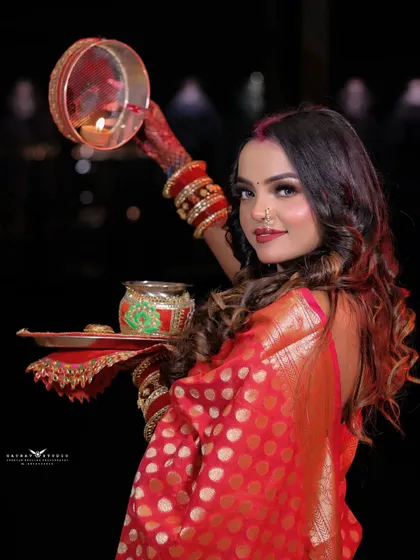 A traditional Karwa Chauth pose, with the model holding the decorative thali and sieve (chhalni). The lighting highlights the festive elements and her serene expression.