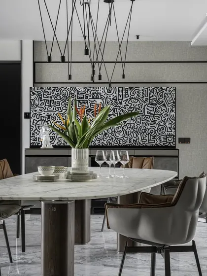A closer look at the dining setup in the Cuffe Parade apartment. The elegant oval marble table is surrounded by comfortable grey leather chairs, all under a striking modern pendant light fixture, creating a chic and cheerful cocoon.
