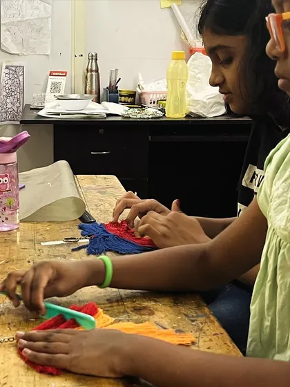 Two students work side-by-side on their macrame keychains. Learning together and sharing tips is a big part of the fun in our group classes.
