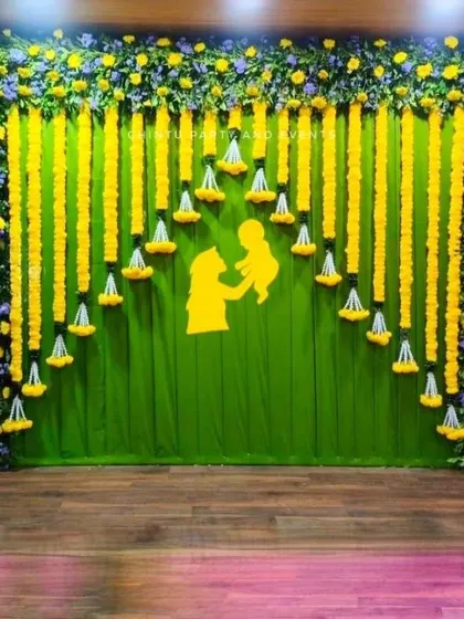 A traditional Seemantham backdrop made of green fabric and marigold flower garlands. A cutout of a mother and child adds a sentimental touch.