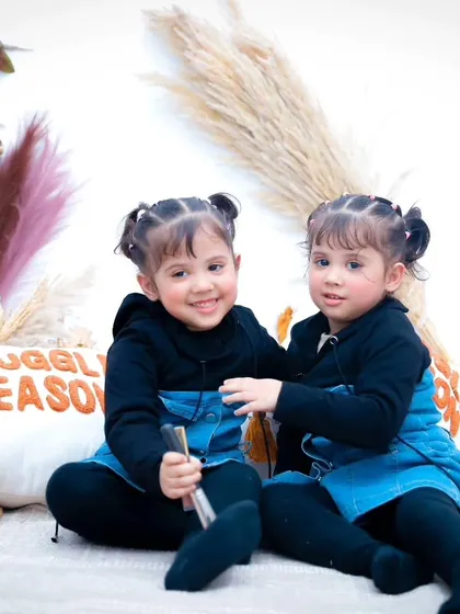The twins posing sweetly on our boho-style studio couch, surrounded by pampas grass and cozy pillows.