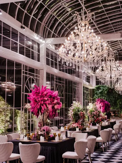 A long shot of the dining area in the glasshouse, with its checkered floor and rows of tables set for a grand feast. The chandeliers and floral arrangements create a breathtaking sense of scale and luxury.