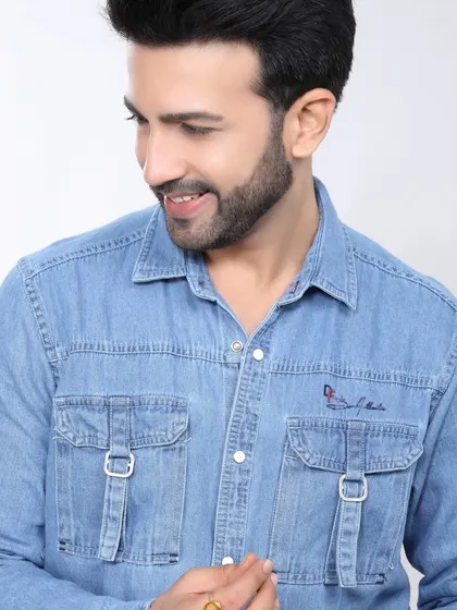 A male model in a light blue denim shirt, smiling and looking away, creating a friendly and approachable vibe for a casual wear brand.
