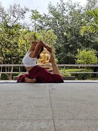 The benefits of King Pigeon Pose are immense, from opening the hips and back to relieving tension. Practicing in a serene outdoor setting with a Buddha statue in the background enhances the sense of calm.