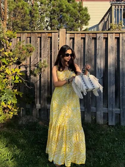 Holding the handbag to accessorize the yellow Jardinvue dress, creating a complete summer look.