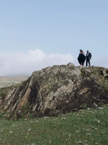 A dramatic wide shot of the couple standing atop a rocky mountain peak, showcasing a sense of adventure and their love story on a grand scale.