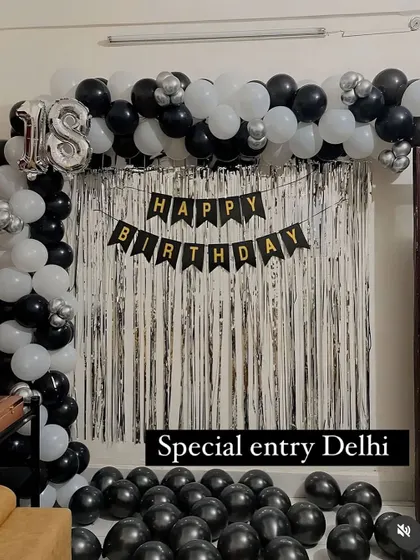 An 18th birthday decoration with a black and white theme. The setup includes a balloon arch, a silver shimmer curtain, and a 'Happy Birthday' banner.